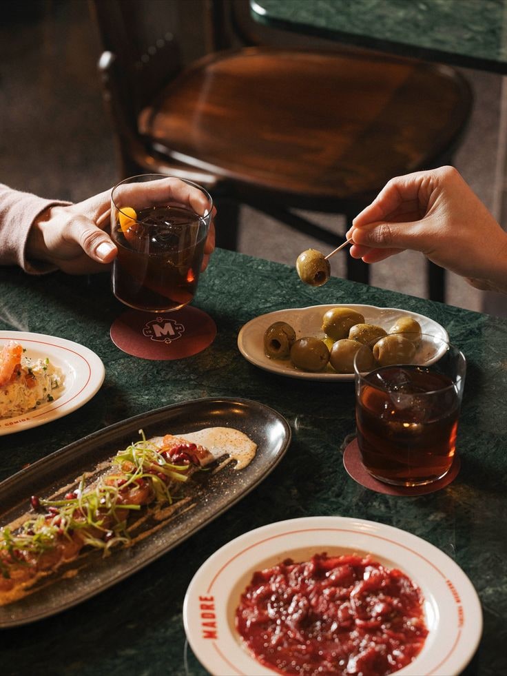 Zwei Gäste stoßen mit Aperitivo an, davor Antipasti-Teller auf grünem Marmor
